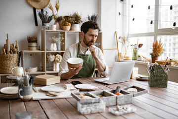 Bearded adult businessman engaged in retail trade of handmade tableware. Young Caucasian man potter...