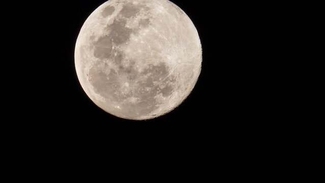 View of a full moon as it moves slowly a little upwards, showing the craters and other landforms that can be seen on the moon's face.
