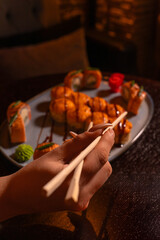 Close-up of a woman's hand holding chopsticks against the background of a blurred sushi dish on a restaurant table. Concept of food. Vertical photo