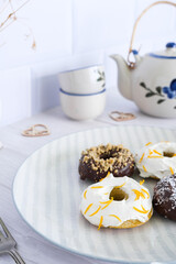 Several homemade donuts are waiting to be eaten at a table with a teapot.