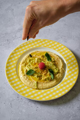 Hand sprinkling pumpkin seeds on a plate of chickpea hummus.