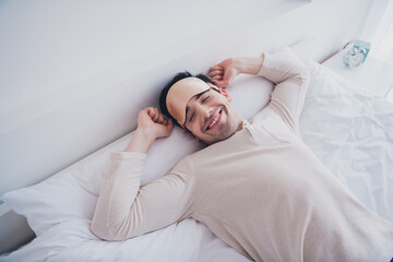 Photo of nice happy man enjoying recreation lying in soft comfortable bed white room interior inside