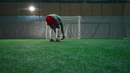 Black soccer player exercising penalty in training hall, scoring goal, back view. Sport training of national team before match and competition, African American man is forward or halfback, empty gate - Powered by Adobe