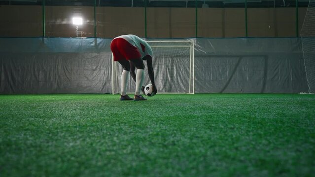 Black soccer player exercising penalty in training hall, scoring goal, back view. Sport training of national team before match and competition, African American man is forward or halfback, empty gate
