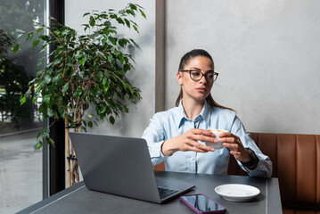 Young tired overworked business woman sitting in a coffee shop with laptop, taking a break from...