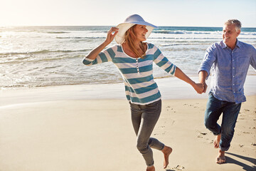 Happy couple, holding hands and running at beach on vacation, travel or summer holiday for love in nature. Mature man, woman and smile at ocean for adventure, support or laughing on date together