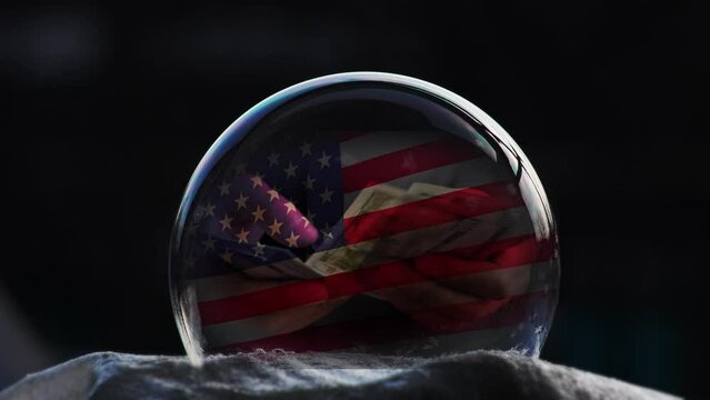 Cg. Hands count US dollar bills against the background of a flag and inside a soap bubble covering a pattern as it freezes on a black background. Inflation and financial bubble