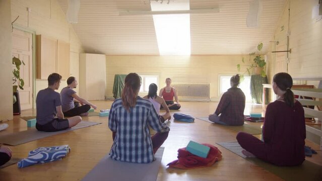 Class sit cross-legged on yoga mats during mindful breathing meditative exercise