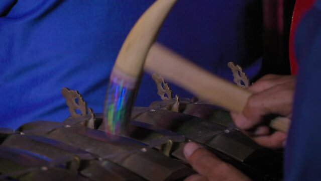A close-up shot of a gamelan performance in Bali, Indonesia, focusing on the musician's hands and the mallet. Shot showcases the craftsmanship and cultural heritage of Balinese musical traditions.