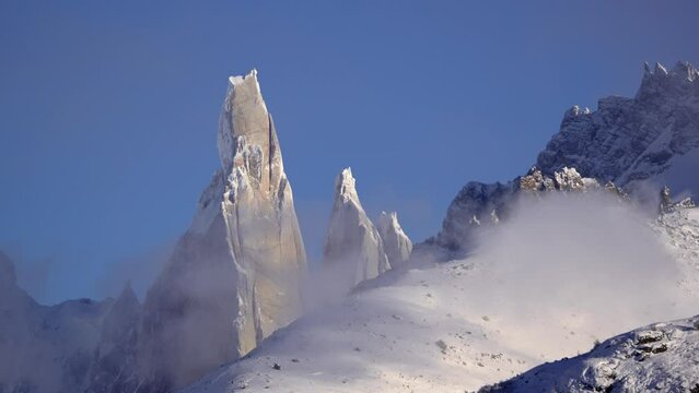 Time lapse shot of dense clouds flying in front of snowy Cerro Torre, Argentina. Blue sky and sunlight in Patagonian nature. Wide shot.