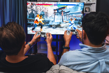 Friend gamers playing video game of battle martial arts fighter on TV using joysticks position of...