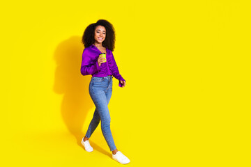 Full body photo of attractive young woman hold paper cup walking dressed stylish violet clothes isolated on yellow color background