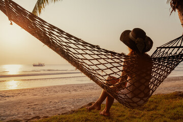 summer vacation travel, calm woman relaxing in hammock at sunset near the sea