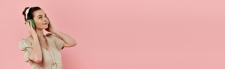 Naklejka premium A young pregnant woman in a dress peacefully speaks on her cell phone against a pink background.