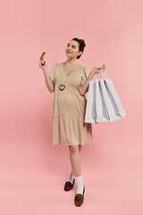 A pregnant woman in a dress holds two bags and a credit card against a vibrant pink background.