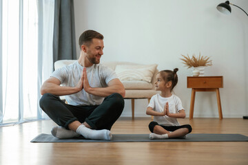 Father with little daughter are doing yoga at home