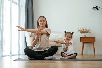 Young woman with little girl are doing yoga at home