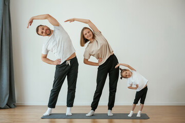 Warm up exercises. Family of mother, father and daughter are doing yoga at home