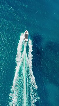 Vertical Screen: Aerial footage captures a speedboat creating a wake in deep blue waters under a sunny sky on a vertical screen. Scene is both dynamic and serene, offering a tranquil yet exciting view