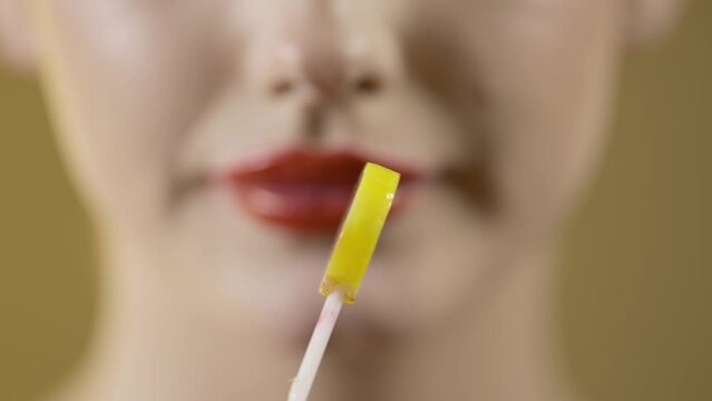 Makro ujęcie kobiety na ż&oacute;łtym tle z intensywnie czerwonymi ustami, bawiącej się lizakiem z wisienkami w środku, oblizywanie, wkładanie do ust i uśmiech, smak, kolor i zmysłowość