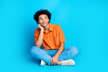 Obraz premium Full length photo of dreamy funny guy wear orange shirt smiling looking emtpy space isolated blue color background