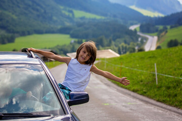 Cute child, boy looking from a car window, travel on the road to scenic mountains