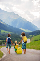 Little children, boy brothers with backpacks and sutcase, travel on the road to scenic mountains,...