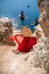 woman in a red dress stands on a cliff overlooking the ocean. The scene is serene and peaceful,...