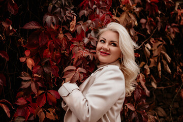 A woman is sitting in a field of red leaves, smelling the foliage. She is wearing a white shirt and...