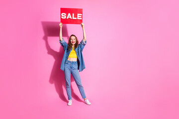 Full length photo of adorable lovely girl wear jeans shirt rising sale placard empty space isolated pink color background