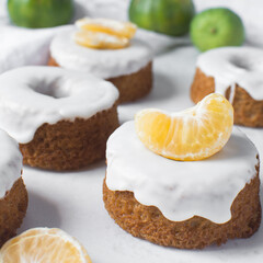 Iced mini bundt cake on a white tray, vanilla bundlette cakeswith a clementine segment on a white background, small vanilla bundt cakes with an icing glaze