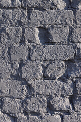 The old chipped brick wall is evenly painted over with gray paint. Close-up.