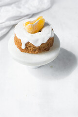 Iced mini bundt cake on a white marble tray, vanilla bundlette with a clementine segment on a plate, small vanilla bundt cake with an icing glaze