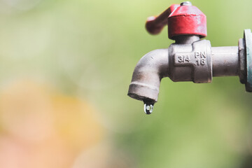 Close-up of a Dripping Outdoor Water Faucet Against a Blurred Natural Background