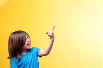 Smiling boy pointing to space for text. Blue t-shirt. Yellow background. Emotions.