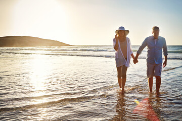 Senior couple, walking and holding hands with beach sunset for love, embrace or bonding together in...