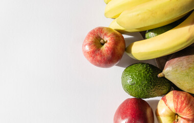 Fruits lie on a white table. Food shopping. Apples, bananas, avocado and mango close-up. Copy space. Top view