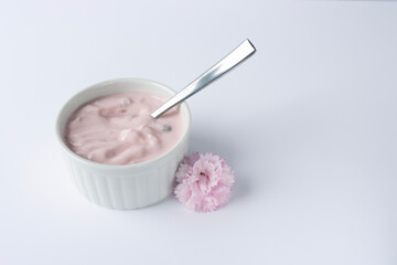 Ramekin with pink yogurt on a white background. Spoon in yogurt. Pink carnation flower. Copy space. Close-up, macro
