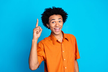 Photo of excited funny guy wear orange shirt pointing finger up emtpy space isolated blue color...