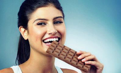 Woman, portrait and happy snack and chocolate for treat and delicious, isolated on blue background. Smile, face and candy, eating with female model in studio and tasting food, dessert or sweets