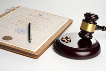 Marriage contract, golden wedding rings and gavel on white background, close-up