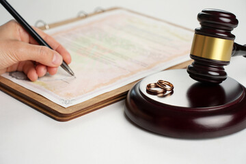 Woman hand signing divorce contract, close-up. Wedding rings with marriage contract and judge gavel...