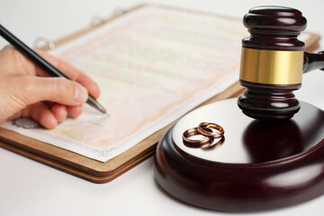 Woman hand signing divorce contract, close-up. Wedding rings with marriage contract and judge gavel...