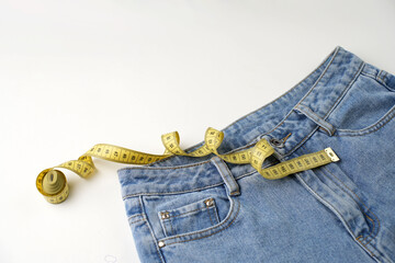 Jeans and measuring tape on a blue background with copy space, close-up. Weight loss and diet...