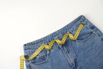 Jeans and measuring tape on a blue background with copy space, close-up. Weight loss and diet...