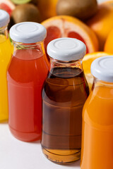 Assortment of fruit juices in glass bottles among fruits on white background