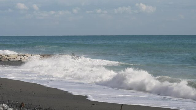 waves crash onto the beach and rocks on a sunny day
