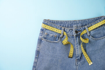 Jeans and measuring tape on a blue background with copy space, close-up. Weight loss and diet concept