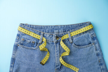 Jeans and measuring tape on a blue background with copy space, close-up. Weight loss and diet concept