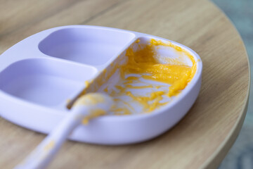 Silicone plate with pumpkins puree on the wooden table. Food for babies. Selective focus.